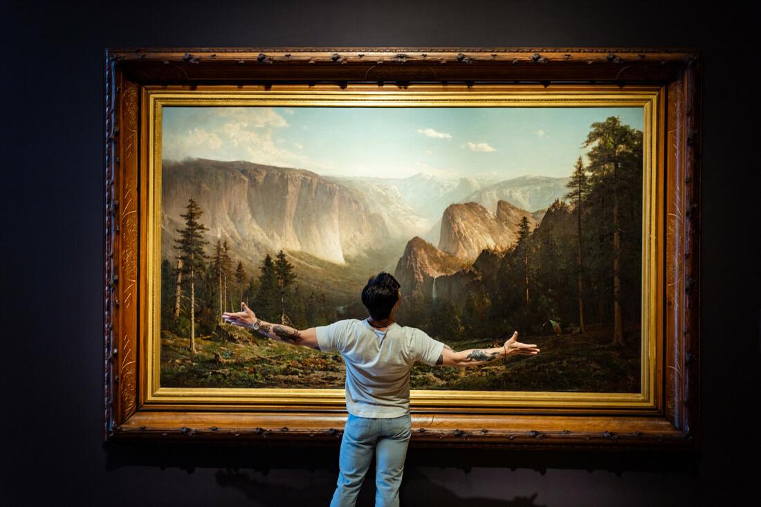 A visitor spreads his arms wide, taking in the view of Thomas Hill's Yosemite.